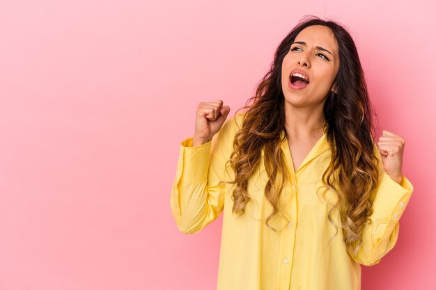 Jovem mulher mexicana isolada na parede rosa, levantando o punho após uma vitória, o conceito de vencedor.