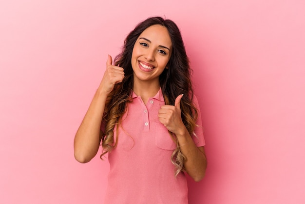 Jovem mulher mexicana isolada na parede rosa, levantando os dois polegares, sorrindo e confiante.