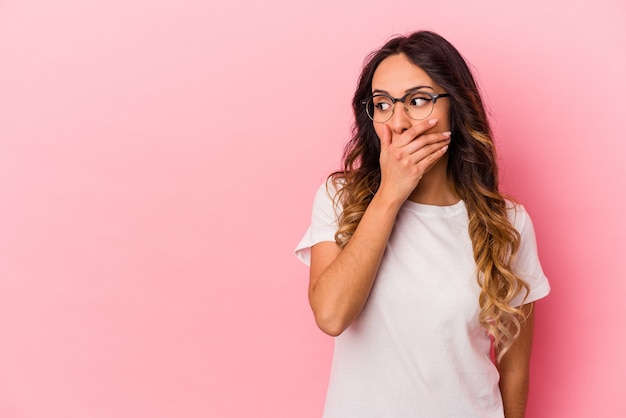 Jovem mulher mexicana isolada na parede rosa pensativa, olhando para um espaço de cópia, cobrindo a boca com a mão.