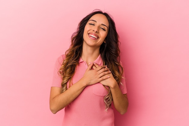 Jovem mulher mexicana isolada na parede rosa rindo mantendo as mãos no coração, o conceito de felicidade.