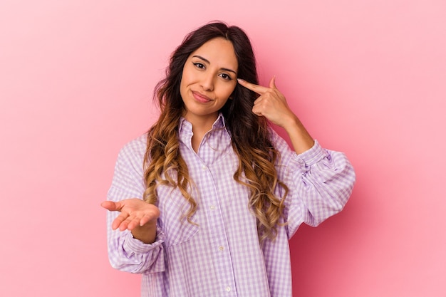 Jovem mulher mexicana isolada na parede rosa, segurando e mostrando um produto por lado.