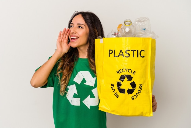 Jovem mulher mexicana reciclando plástico isolado no fundo branco, gritando e segurando a palma da mão perto da boca aberta.