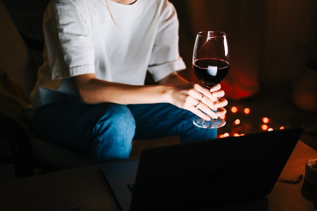 Jovem mulher milenar com videochamada no laptop e bebendo vinho, usa a tecnologia para se comunicar com amigos ou família.