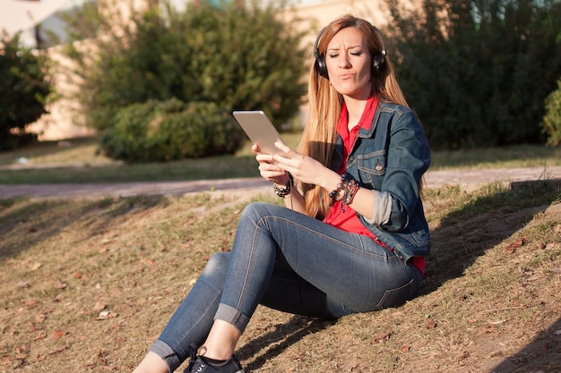 Foto jovem, mulher moderna, ouvindo música com fones de ouvido e smartphone, sorrindo ao ar livre no parque