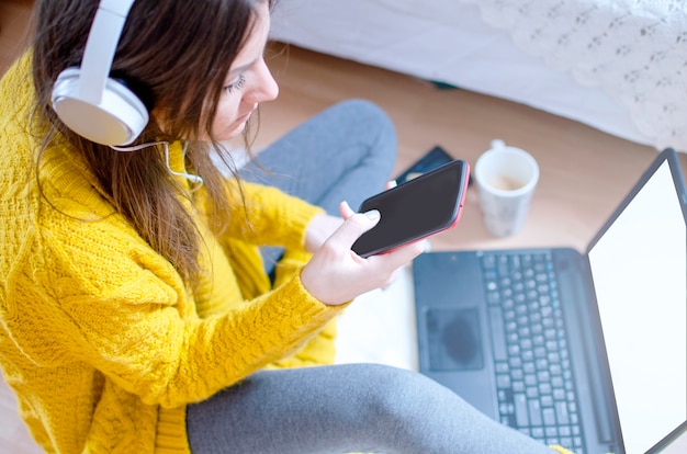 Foto jovem mulher moderna sentada no chão no quarto e usando o telefone para fazer compras on-line com cartão de crédito