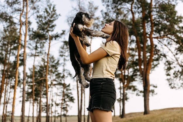 Jovem mulher morena segurando em braços um cão de raça schnauzer em miniatura brincando com ele