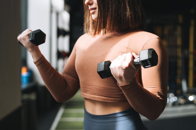 Jovem mulher morena treinando seus músculos com halteres no ginásio do clube de fitness