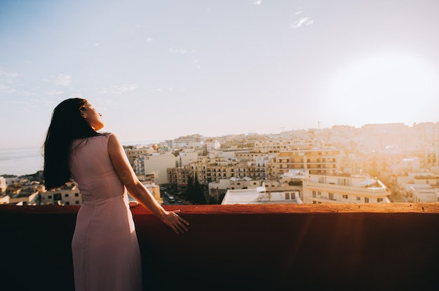 Jovem mulher moreno bonita em um vestido de noite branco. cenário pôr do sol cenário da cidade.