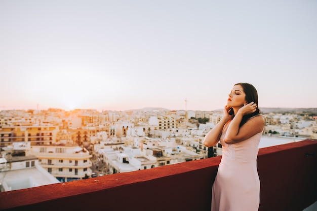 Jovem mulher moreno bonita em um vestido de noite branco. cenário pôr do sol cenário da cidade.