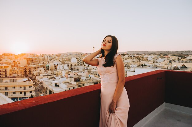 Jovem mulher moreno bonita em um vestido de noite branco. cenário pôr do sol cenário da cidade.