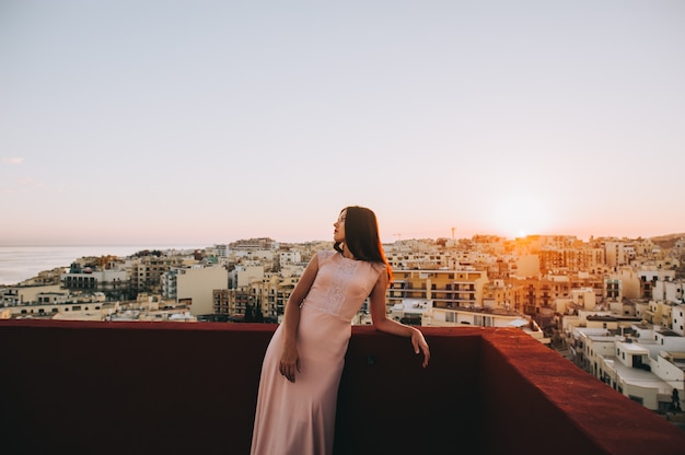 Jovem mulher moreno bonita em um vestido de noite branco. cenário pôr do sol cenário da cidade.