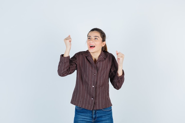 Jovem mulher mostrando o gesto do vencedor em uma camisa listrada, jeans e parecendo com sorte. vista frontal.