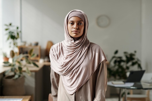 Jovem mulher muçulmana bonita com lenço de cabeça bege e camisola olhando para a câmera