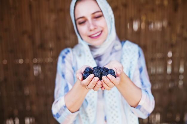 Jovem mulher muçulmana em hijab segurando tâmaras nas mãos