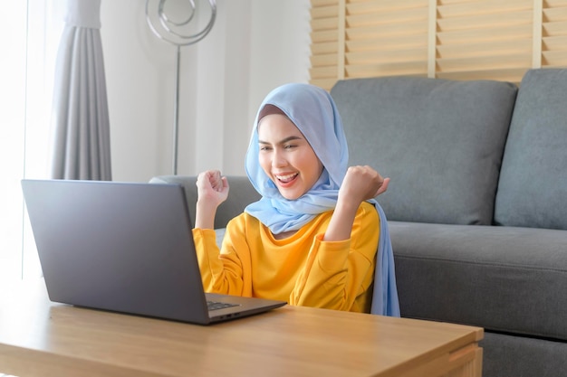 Jovem mulher muçulmana feliz trabalhando no laptop na sala de estar em casa