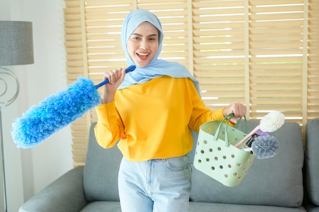 Jovem mulher muçulmana feliz usando luvas amarelas e segurando uma cesta de limpeza