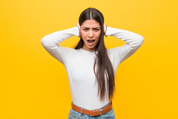 Jovem mulher muito árabe contra um amarelo cobrindo as orelhas com as mãos, tentando não ouvir o som muito alto.