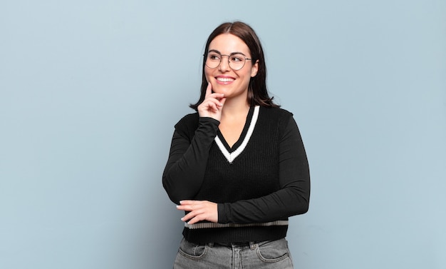 Jovem mulher muito casual sorrindo feliz e sonhando acordada ou duvidando, olhando para o lado