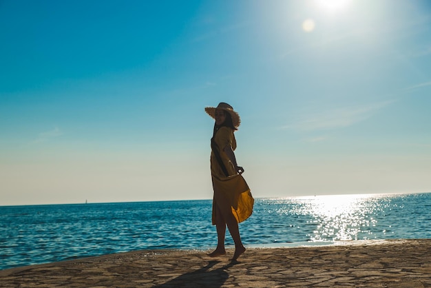 Jovem mulher muito sorridente em vestido amarelo andando pela praia de pedra