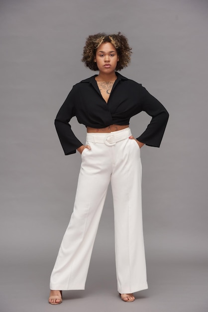 Jovem mulher multiétnica confiante em blusa preta cortada e calça branca