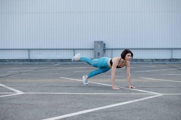 Jovem mulher muscular fazendo exercícios de núcleo. Ajuste feminino fazendo flexões durante o treino ao ar livre.