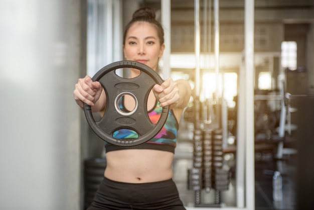 Foto jovem mulher muscular que levanta peso no gym.