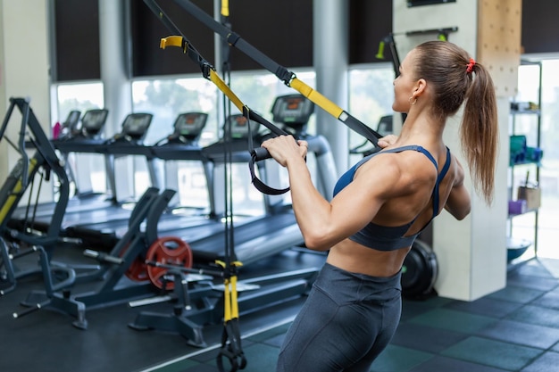 Jovem mulher musculosa atraente em roupas esportivas treina músculos com sistema de resistência trx em uma academia moderna. Treinamento cruzado. Fitness moderno