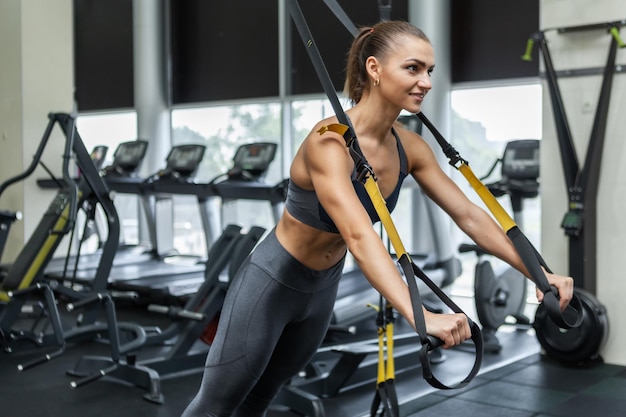 Jovem mulher musculosa atraente em roupas esportivas treina músculos com sistema de resistência trx em uma academia moderna. Treinamento cruzado. Fitness moderno