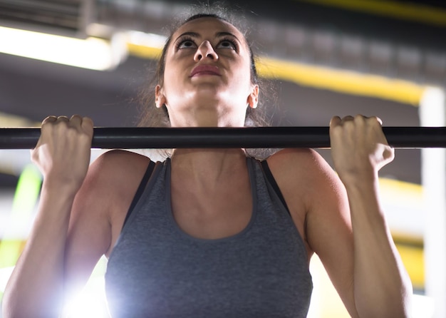 Jovem mulher musculosa fazendo pull ups na barra horizontal como parte do cross fitness training