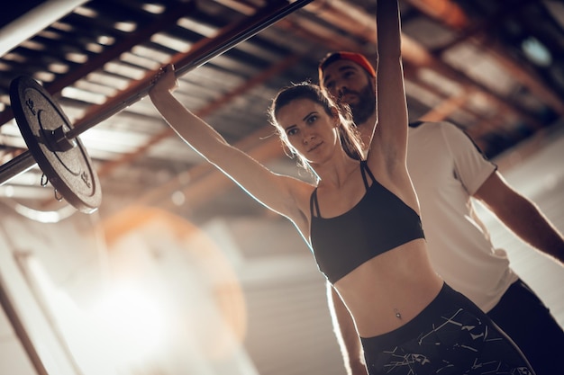 Jovem mulher musculosa fazendo treino cruzado com um personal trainer no ginásio da garagem.