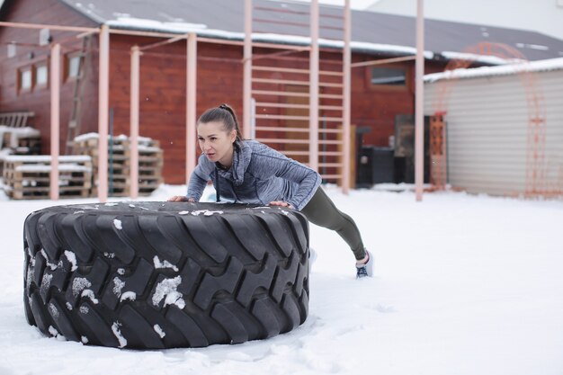 Jovem mulher musculosa treinando com pneu pesado, ao ar livre