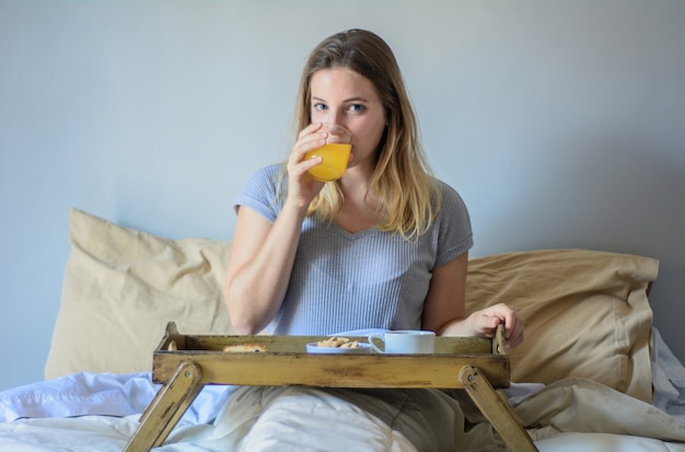 Jovem mulher na cama tomando café da manhã