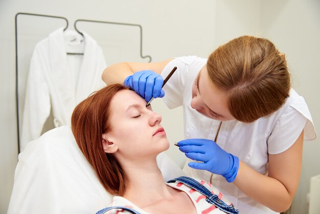 Jovem mulher na correção de sobrancelha na clínica de cosmetologia