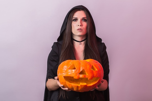Jovem mulher na fantasia de bruxa de Halloween em estúdio com abóbora amarela.