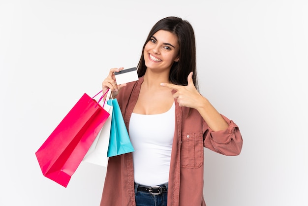 Jovem mulher na parede branca segurando sacolas de compras e um cartão de crédito