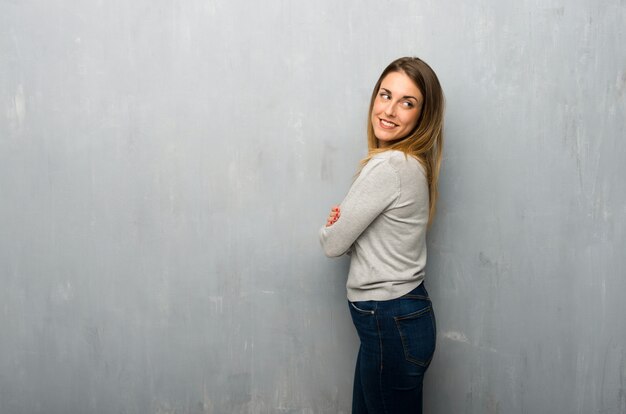 Jovem mulher na parede texturizada, olhando por cima do ombro com um sorriso