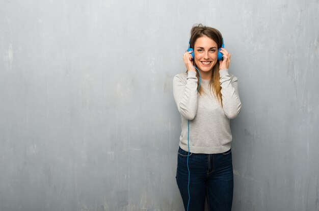 Jovem mulher na parede texturizada ouvindo música com fones de ouvido