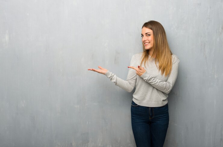 Foto jovem mulher na parede texturizada segurando copyspace imaginário na palma da mão para inserir um anúncio