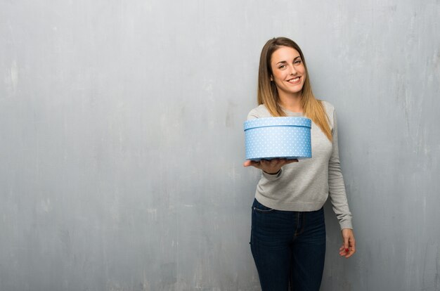 Jovem mulher na parede texturizada segurando um presente nas mãos