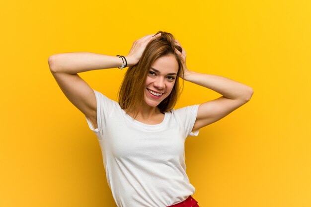 Jovem mulher natural ri alegremente, mantendo as mãos na cabeça