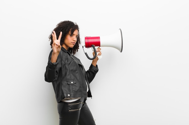 Jovem mulher negra com um megafone, vestindo uma jaqueta de couro contra parede branca