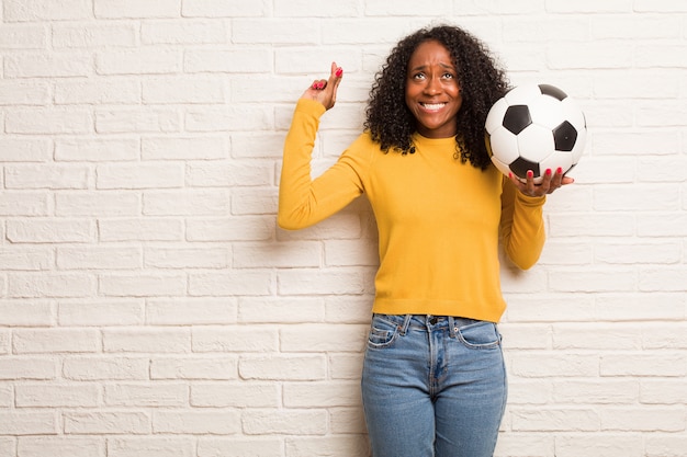 Jovem mulher negra cruzando os dedos, deseja ter sorte para projetos futuros, excitada mas preocupada, expressão nervosa, fechando os olhos