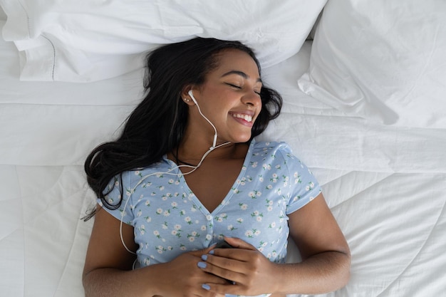 Foto jovem mulher negra em sua cama ouvindo música com fones de ouvido em casa se sentir bem