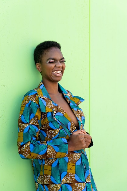 Jovem mulher negra em um pedaço de tecido tradicional africano sorrindo contra um fundo de pistache