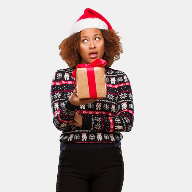 Jovem mulher negra segurando um presente no dia de Natal cansado e entediado