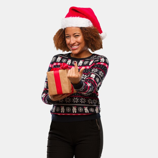 Jovem mulher negra segurando um presente no dia de Natal, convidando a vir