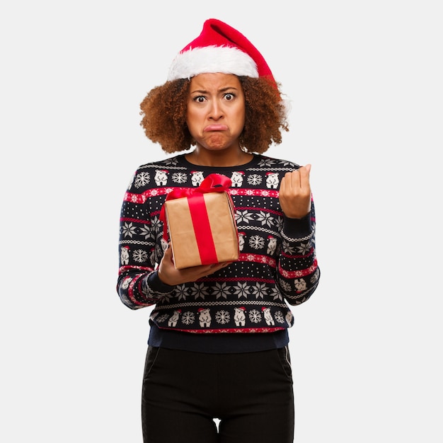 Jovem mulher negra segurando um presente no dia de Natal, fazendo um gesto de necessidade