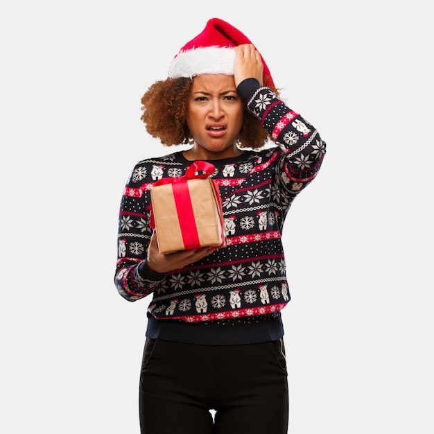 Jovem mulher negra segurando um presente no dia de Natal preocupado e oprimido