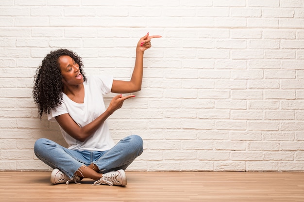 Jovem mulher negra sentada num chão de madeira, apontando para o lado