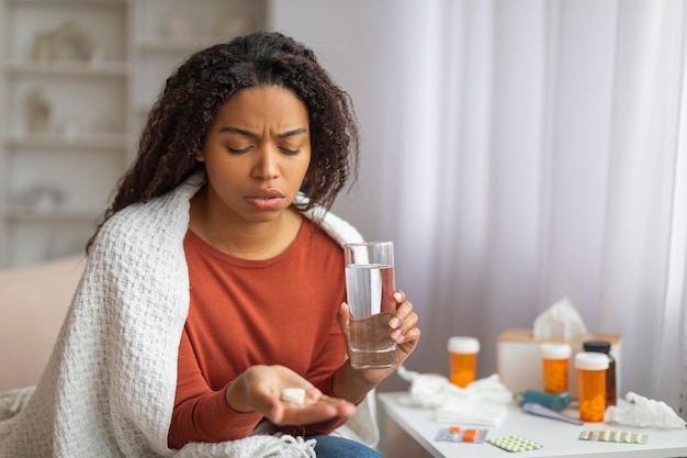 Foto jovem mulher negra tomando medicação em casa durante o dia